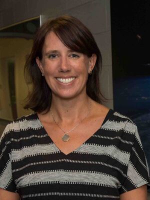 Sarah Ringerud smiles in front of a dark backdrop, wearing a striped t-shirt