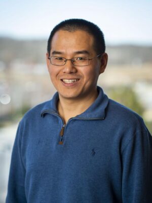 Yalei You smiles in front of a colorful backdrop, wearing a blue polo shirt