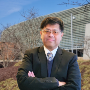 The headshot of Dr. Shu-peng Ho; He wears a suit with his arms crossed in front of a wintery NOAA building