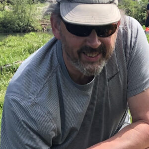 Dr. Jay Mace in the field, wearing a ball cap and sunglasses