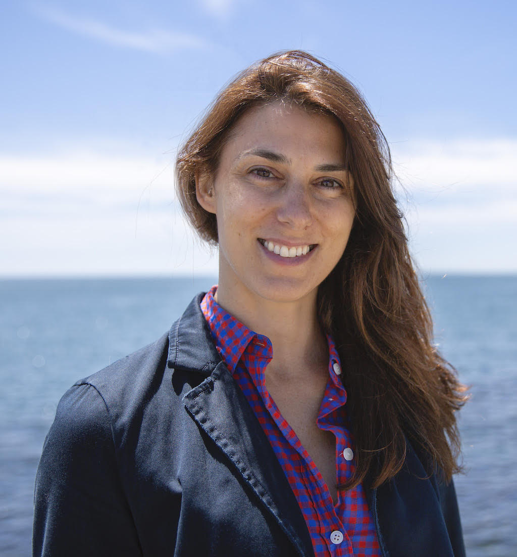 The headshot of Dr. Kelly Lombardo, in front of the ocean