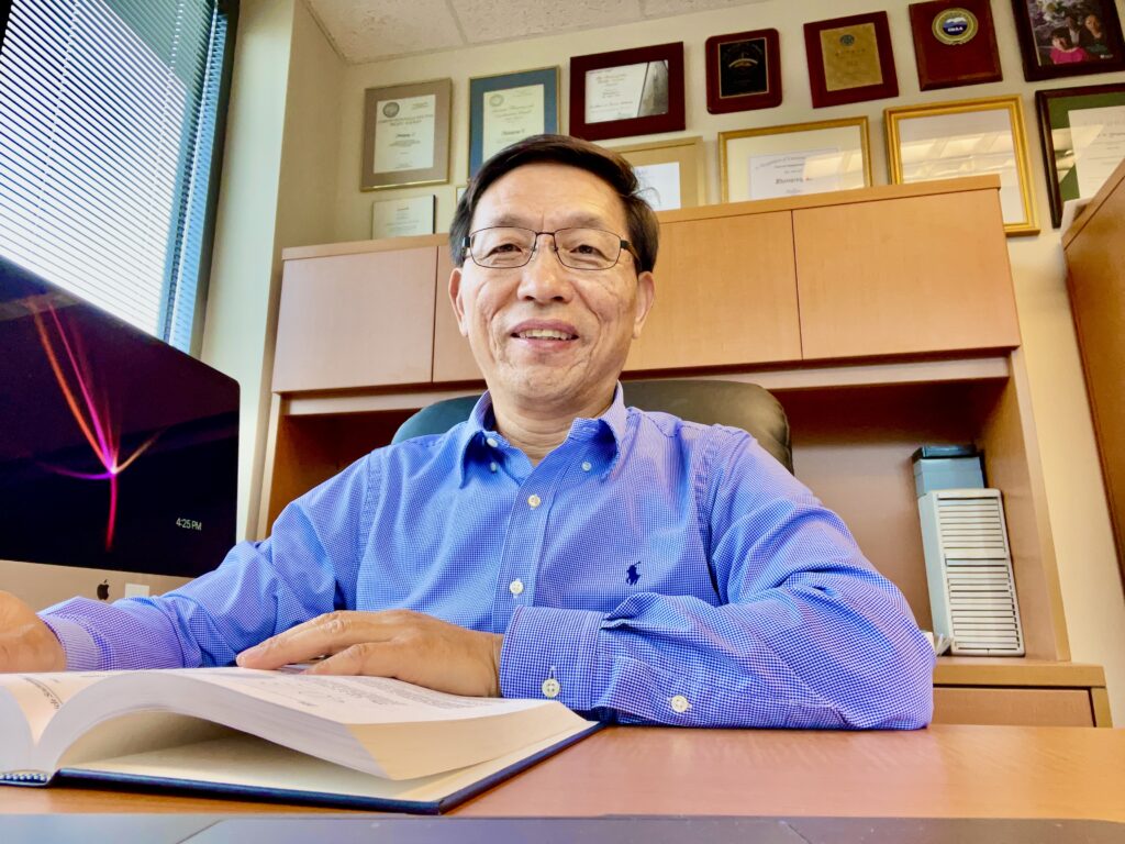 Dr. Li smiles over a book on his desk